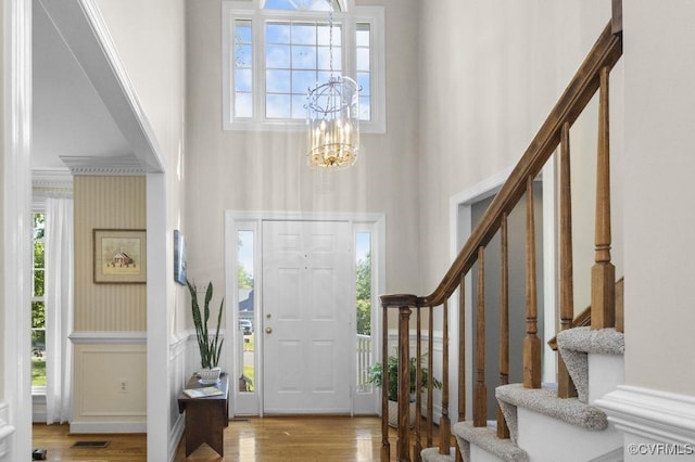 entryway featuring a towering ceiling, a chandelier, stairs, wood finished floors, and healthy amount of natural light