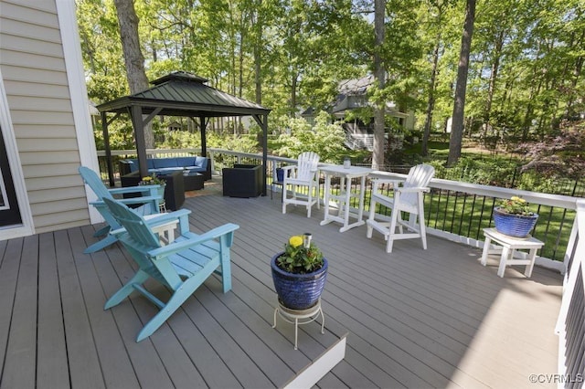 wooden deck with an outdoor hangout area, a gazebo, and view of wooded area