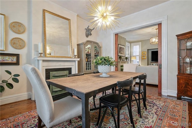 dining room with a chandelier, wood finished floors, baseboards, a fireplace, and ornamental molding