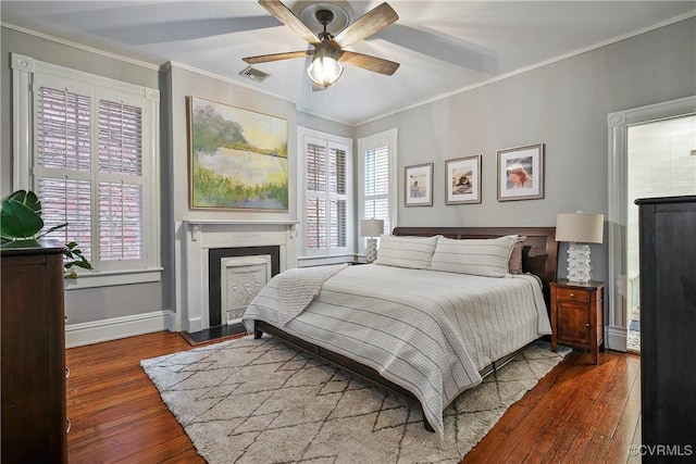 bedroom featuring hardwood / wood-style flooring, crown molding, baseboards, a fireplace with raised hearth, and a ceiling fan
