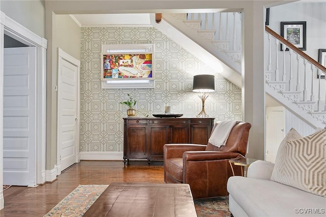 sitting room featuring wallpapered walls, baseboards, stairway, dark wood-style floors, and crown molding