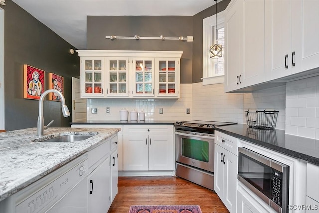kitchen featuring appliances with stainless steel finishes, a sink, white cabinets, backsplash, and glass insert cabinets