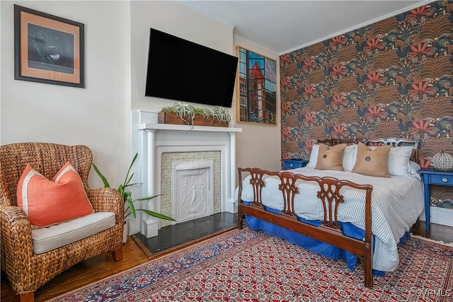 bedroom with ornamental molding, wood finished floors, and a fireplace with raised hearth