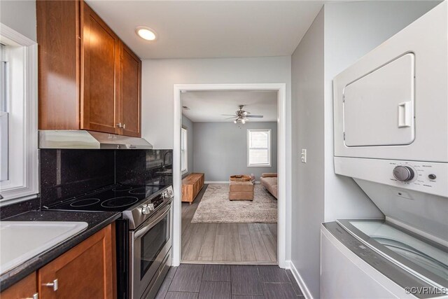 25 Cherry St, Petersburg, VA 23803 - kitchen with stainless steel electric stove, stacked washer / drying machine, under cabinet range hood, brown cabinets, and baseboards