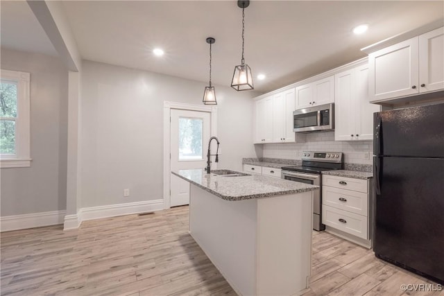 kitchen with stainless steel appliances, a sink, light wood finished floors, decorative backsplash, and light stone counters