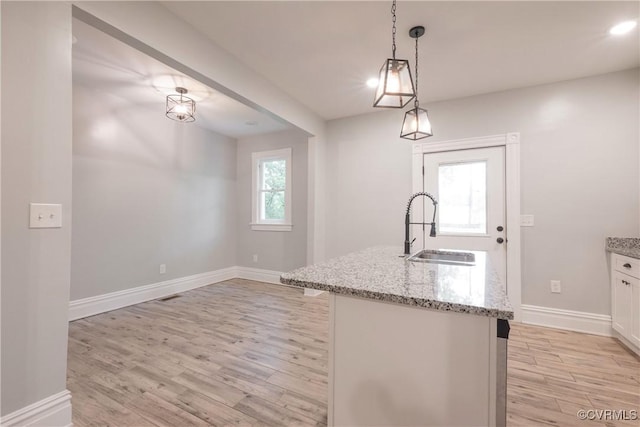 kitchen featuring a sink, light wood-style floors, light stone counters, baseboards, and hanging light fixtures