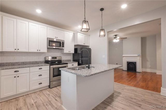 kitchen with appliances with stainless steel finishes, a sink, light wood-style floors, backsplash, and ceiling fan