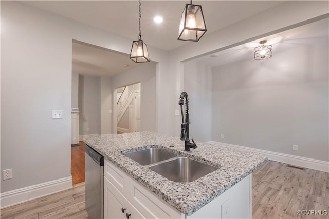 kitchen with stainless steel dishwasher, light wood finished floors, white cabinets, a sink, and pendant lighting