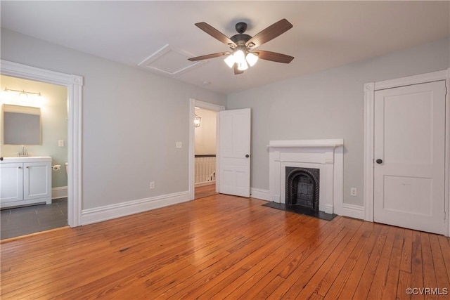 unfurnished living room with hardwood / wood-style flooring, a fireplace, baseboards, ceiling fan, and attic access