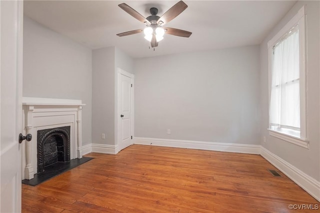 unfurnished living room with wood finished floors, a fireplace, a ceiling fan, and baseboards