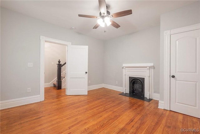 unfurnished living room featuring ceiling fan, a fireplace with raised hearth, light wood-style floors, baseboards, and stairs