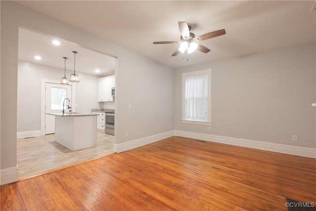 unfurnished living room with light wood-style flooring, a ceiling fan, baseboards, recessed lighting, and a sink
