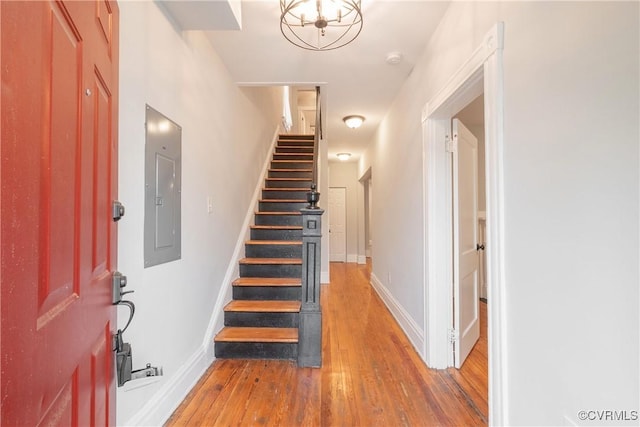 foyer featuring electric panel, light wood-style floors, stairway, a chandelier, and baseboards