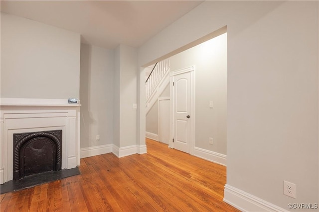 unfurnished living room featuring wood-type flooring, baseboards, a fireplace, and stairs
