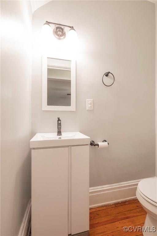 half bathroom with toilet, wood finished floors, and vanity