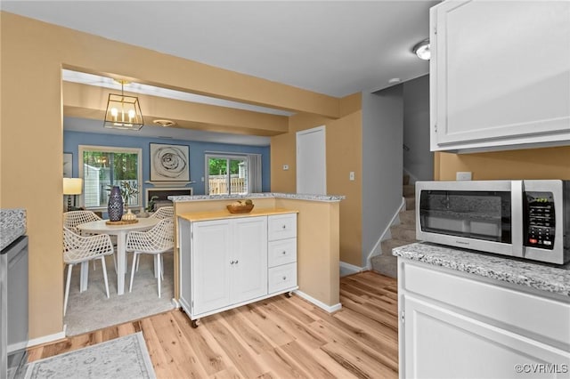 kitchen with light wood-style floors, white cabinets, pendant lighting, baseboards, and light stone countertops