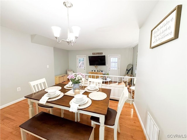 dining area with light wood-style flooring, a chandelier, and baseboards