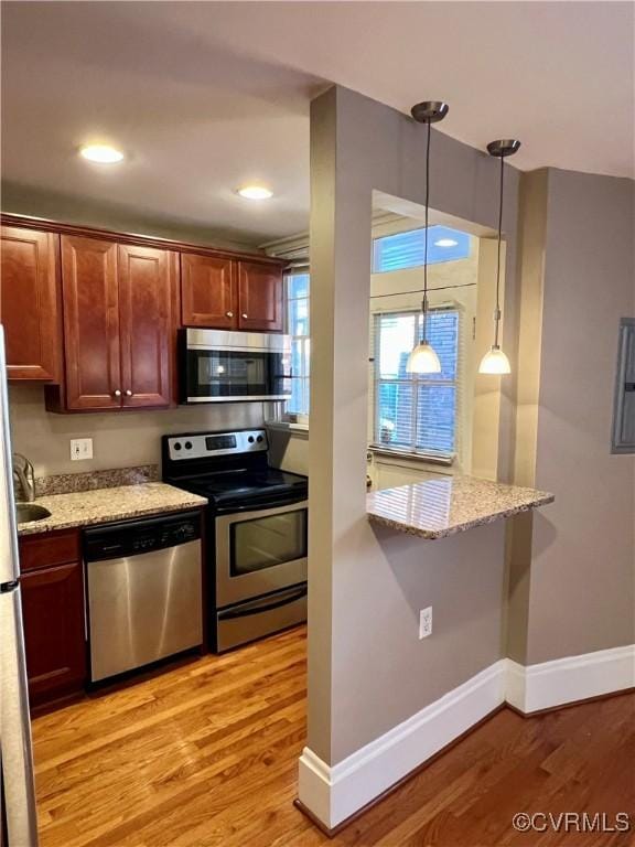 kitchen featuring stainless steel appliances, light wood-style floors, baseboards, light stone countertops, and hanging light fixtures