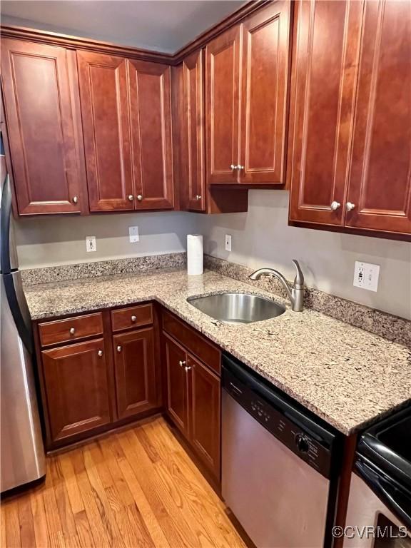 kitchen with appliances with stainless steel finishes, a sink, light wood-style floors, and light stone countertops
