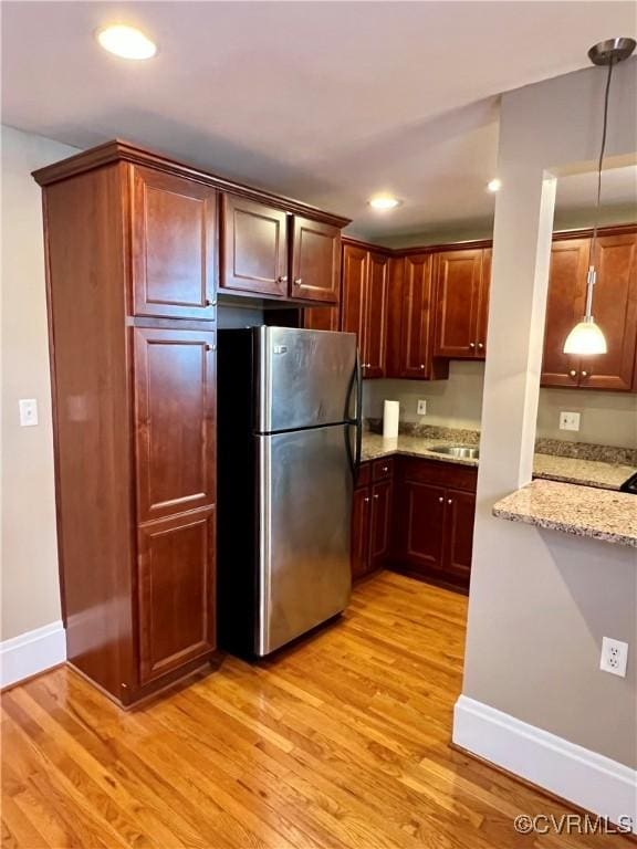 kitchen featuring freestanding refrigerator, light wood-style floors, light stone countertops, baseboards, and pendant lighting