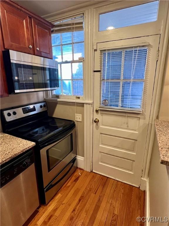 kitchen with stainless steel appliances, light wood-type flooring, and light stone countertops