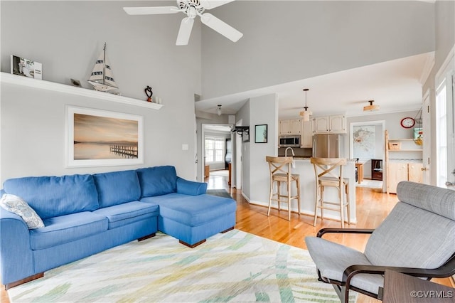 living room with light wood finished floors, a ceiling fan, and a high ceiling