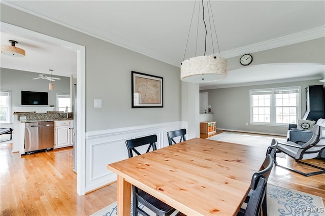 dining area with crown molding, ceiling fan, light wood finished floors, and a wainscoted wall