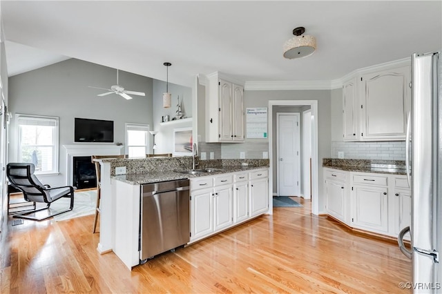kitchen with appliances with stainless steel finishes, a sink, a fireplace, white cabinets, and vaulted ceiling