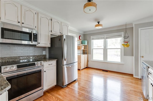 kitchen with appliances with stainless steel finishes, crown molding, light wood-style flooring, light stone countertops, and a wainscoted wall