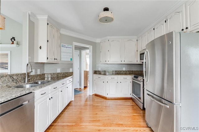 kitchen featuring stainless steel appliances, a sink, white cabinetry, light stone counters, and light wood-style flooring