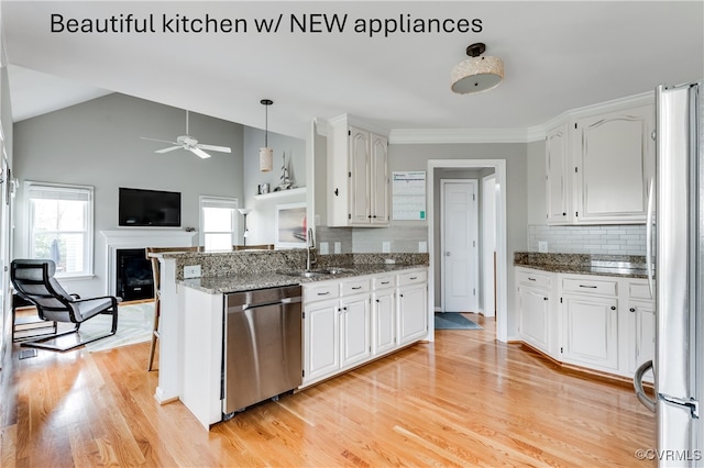 kitchen featuring stainless steel appliances, a sink, a fireplace, white cabinetry, and vaulted ceiling