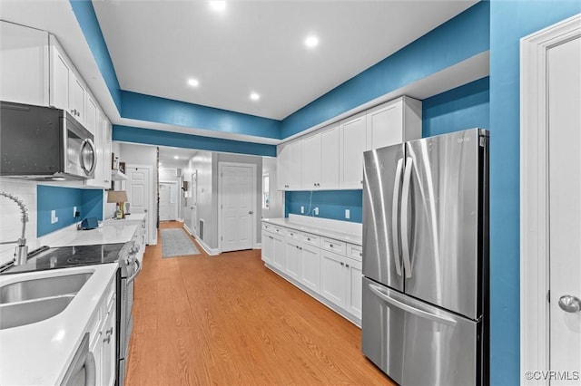 1415 N 25th St, Richmond, VA 23223 - kitchen featuring appliances with stainless steel finishes, white cabinetry, light wood-style flooring, light countertops, and a sink