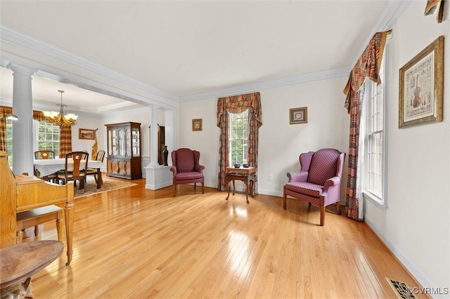 living area featuring decorative columns, light wood-style flooring, a chandelier, ornamental molding, and baseboards