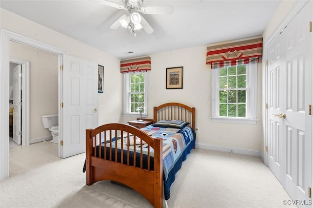 bedroom with light carpet, baseboards, a ceiling fan, and ensuite bath