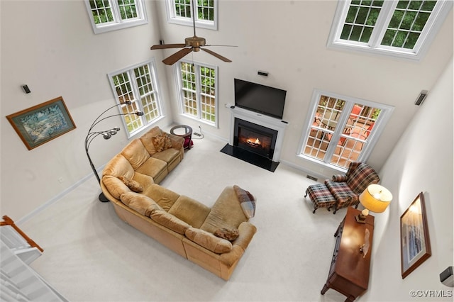 carpeted living room with a high ceiling, a fireplace with flush hearth, a ceiling fan, and baseboards