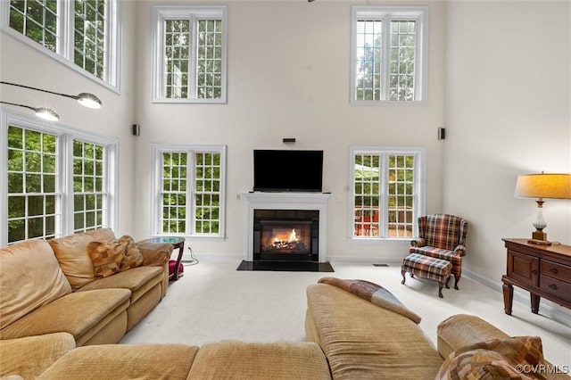 carpeted living room with a towering ceiling, a fireplace with flush hearth, and baseboards