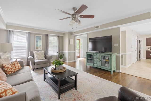 living area with a ceiling fan, ornamental molding, baseboards, and wood finished floors