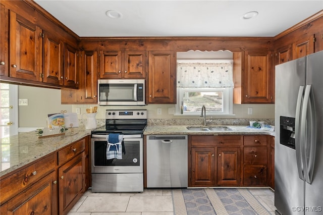 kitchen with appliances with stainless steel finishes, a sink, light stone counters, and light tile patterned floors