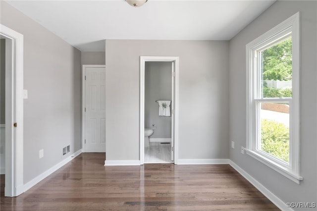 unfurnished bedroom featuring wood finished floors, multiple windows, baseboards, and ensuite bath