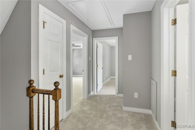 corridor featuring attic access, light colored carpet, and baseboards