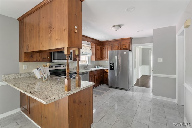 kitchen featuring appliances with stainless steel finishes, a sink, a peninsula, light stone counters, and backsplash