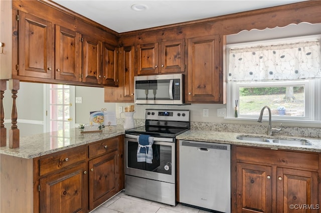 kitchen featuring stainless steel appliances, a sink, a peninsula, light tile patterned flooring, and light stone counters