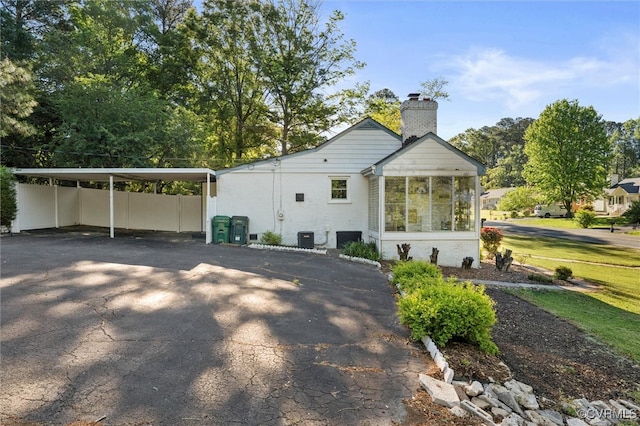 back of house with driveway, a carport, a chimney, brick siding, and fence