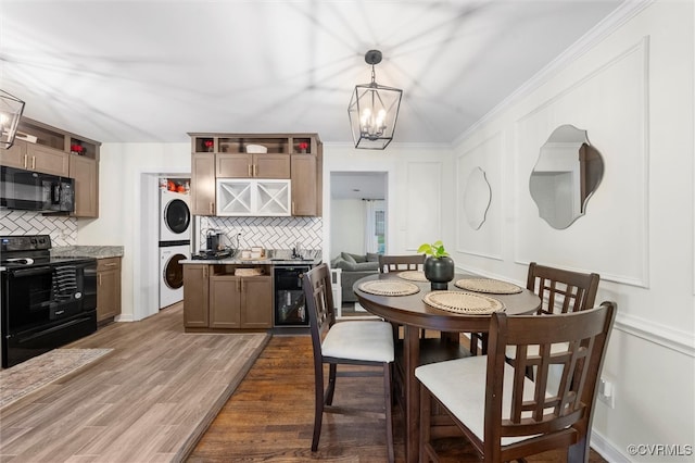 dining room with stacked washing machine and dryer, a chandelier, a decorative wall, and wood finished floors