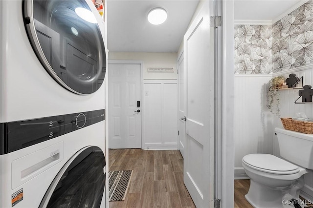 laundry room with stacked washing machine and dryer, wood finished floors, and wallpapered walls