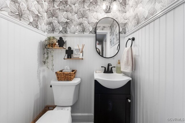 bathroom with toilet, vanity, and wallpapered walls
