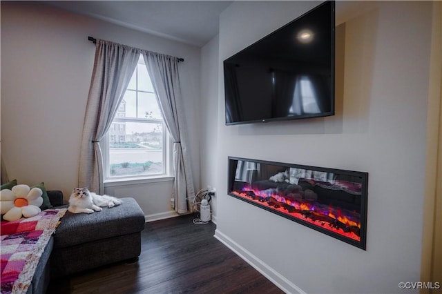 sitting room with dark wood-type flooring, a glass covered fireplace, and baseboards