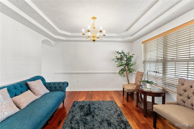living area with a tray ceiling, a chandelier, wood finished floors, and a textured ceiling
