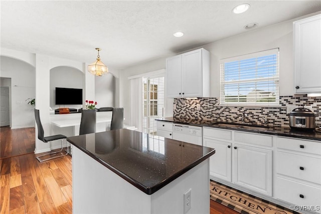 kitchen featuring a sink, white dishwasher, tasteful backsplash, white cabinetry, and a center island