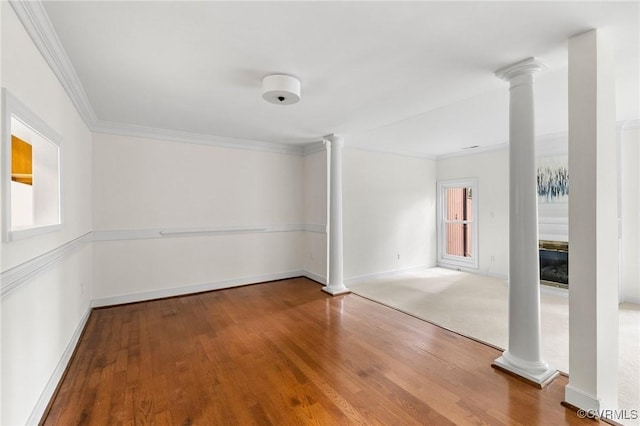 empty room with decorative columns, wood finished floors, baseboards, and crown molding
